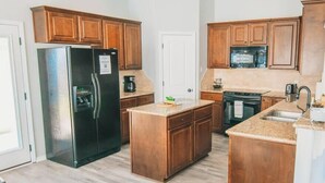 A kitchen with wooden cabinets, a stainless steel refrigerator, a microwave, and a stove. - Spark Getaways: The Golden Lotus Spa, Sauna, EV Charging (Lubbock)