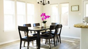 A dining area with a round table, six chairs, and a vase of pink flowers. - Spark Getaways: The Golden Lotus Spa, Sauna, EV Charging (Lubbock)