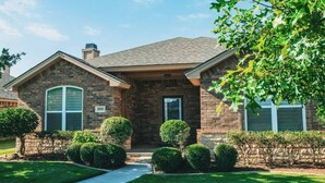 A two-story house with a brick exterior, a front porch, and a well-maintained lawn. - Spark Getaways: The Golden Lotus Spa, Sauna, EV Charging (Lubbock)