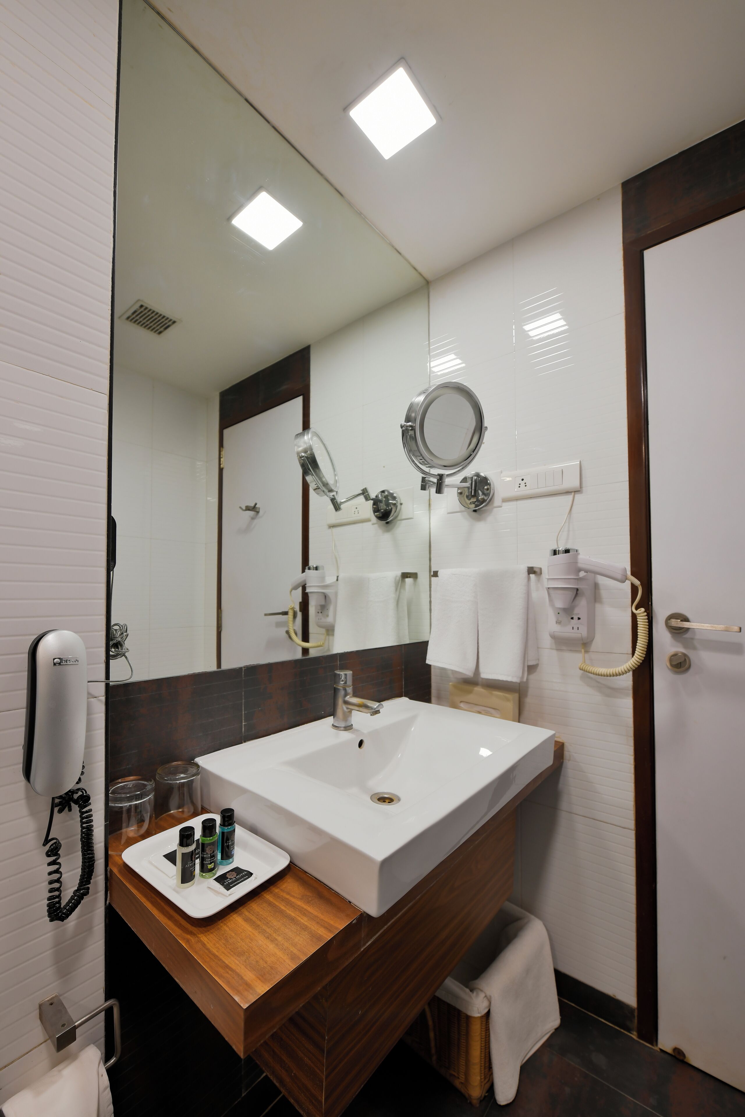 A modern bathroom with a large mirror, white sink, and a vanity with a wooden countertop.