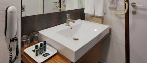 A modern bathroom with a large mirror, white sink, and a vanity with a wooden countertop.