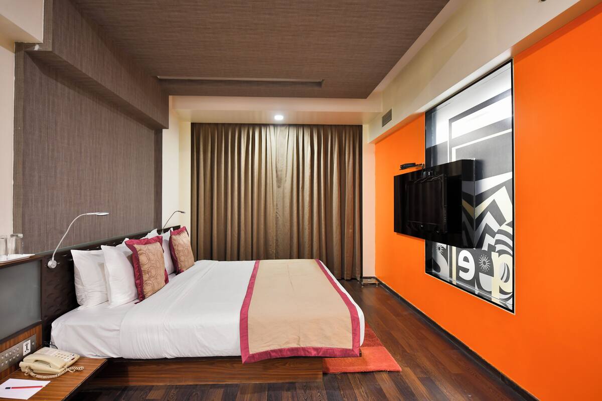 Habitación de hotel con cama, escritorio y teléfono, y televisor montado en la pared.