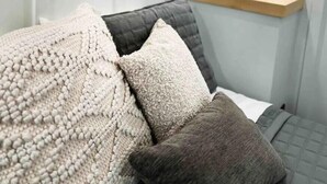 Una camera da letto moderna con un letto, cuscini, un comodino con una pianta e una mensola.