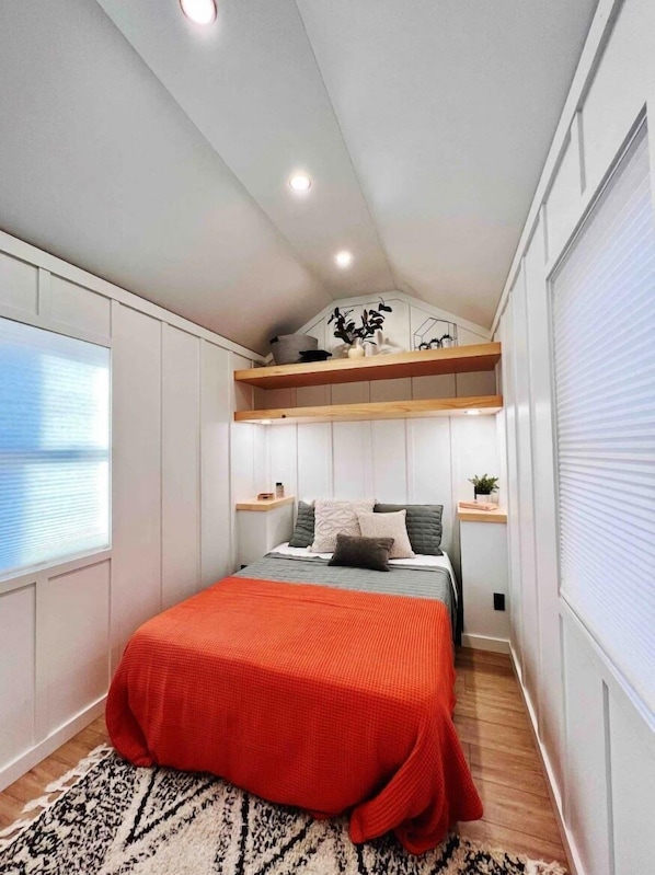 A bedroom with a bed, a red blanket, a window, and built-in shelving. - Unique tiny home experience in a one of a kind tiny home community! (Elizabethtown)
