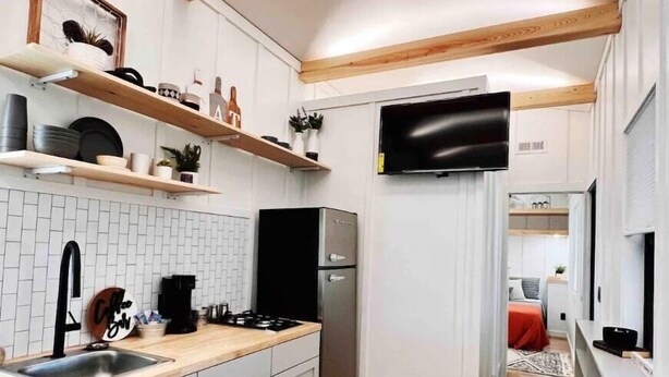Una cucina moderna con mobili bianchi, travi in legno, piano cottura integrato e frigorifero.