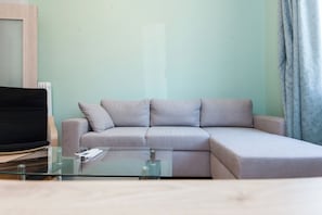 Uma sala de estar moderna com um sofá modular cinza, uma mesa de centro de vidro e uma TV de tela plana.