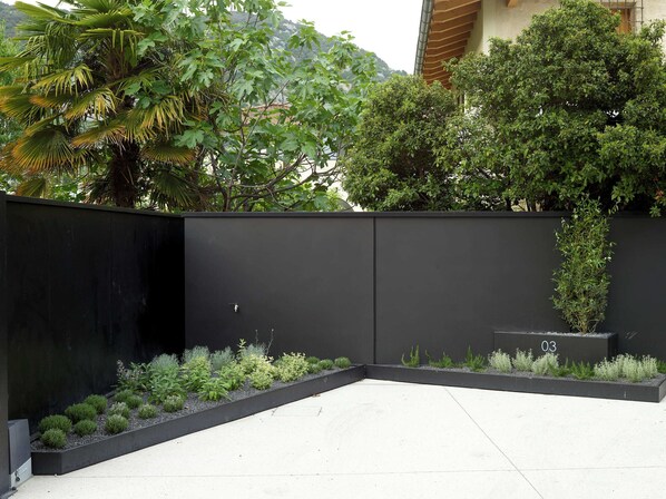 A modern outdoor space with a black fence, a variety of plants, and a number '03' sign. - An outdoor paradise (Arco)