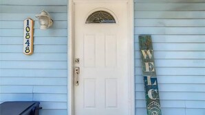 A front door with a number sign, a welcome sign, and a lantern on the wall.
