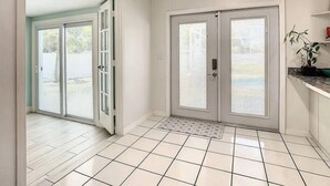 A clean, modern hallway with a tiled floor, double doors, and a small potted plant on a shelf.