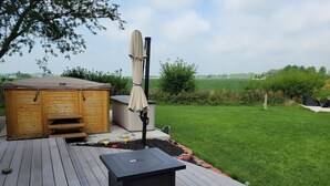 Een houten terras met een zwarte tafel, een houten tuinhuis en een overdekte parasol.