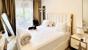 A hotel room with a large bed, a bedside table with a lamp, a mirror, and a view of the outdoors through the window. - 156 Av. Pasteur b1 (Le Blanc-Mesnil)