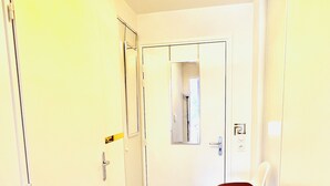 A narrow hallway with a wooden floor, a black doormat, a white door, and a mirror on the wall. - 156 Av. Pasteur b1 (Le Blanc-Mesnil)