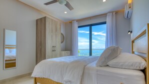 A bedroom with a large bed, a ceiling fan, a view of the sea, and a wardrobe. - Mountainside Retreat Exquisite OceanViews Sleeps6 (Tarcoles)