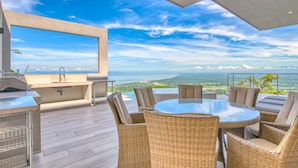A rooftop terrace with a glass table and wicker chairs, overlooking a scenic landscape. - Mountainside Retreat Exquisite OceanViews Sleeps6 (Tarcoles)