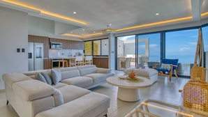 A modern living room with a large sectional sofa, a round coffee table, and a dining area with a kitchen in the background. - Mountainside Retreat Exquisite OceanViews Sleeps6 (Tarcoles)