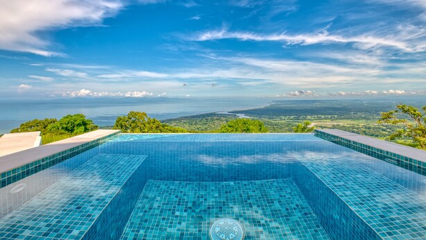 A infinity pool with a clear view of the ocean and distant land. - Mountainside Retreat Exquisite OceanViews Sleeps6 (Tarcoles)