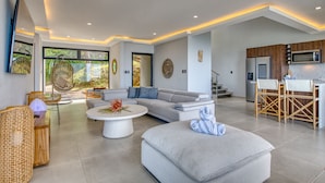 A modern living room with a sofa, coffee table, and a dining area with chairs. - Mountainside Retreat Exquisite OceanViews Sleeps6 (Tarcoles)