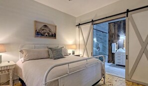 A bedroom with a bed, bedside tables, a painting, and a sliding glass door leading to a bathroom. - Lake Burton - Timpson Cove Luxury Cottage   (Clayton)