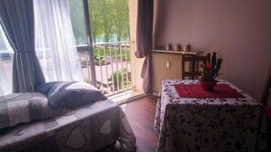 Een kamer met twee bedden, een tafel met een rode placemat, een potplant en uitzicht op het buiten.