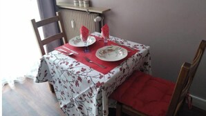 Een eettafel gedekt met borden, bestek en servetten, met een radiator erboven en een raam aan de linkerkant.