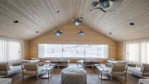 Una habitación moderna y espaciosa con pisos y paredes de madera, ventanas amplias y un alto techo con ventiladores únicos.