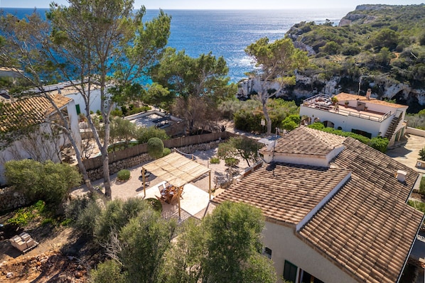 Une propriété située sur la côte, dotée d’un toit en tuiles de terre cuite, d’une terrasse avec mobilier d’extérieur et offrant une vue sur la mer.