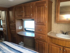 Compact bathroom with sink, mirror, and window, featuring wooden cabinets for storage.