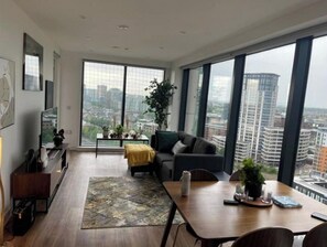 Enjoy a panoramic city view from the large window in this stylish living room with a sofa, coffee table, and dining area.