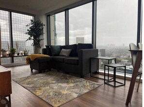 Relax in this stylish living room with a panoramic city view, a comfortable sofa, and a cozy wooden chair.