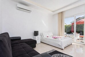 Ein modernes Hotelzimmer mit Bett, einer Couch, einem Fernseher und einem Balkon mit Gartenmöbeln.