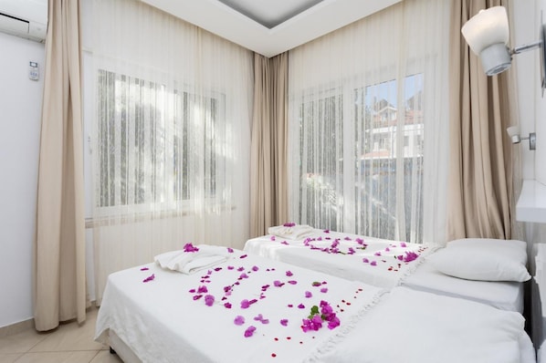 Habitació d'hotel amb dos llits, cortines translúcides, una làmpada al sostre i vista cap a l'exterior.