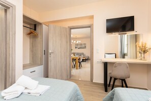 Ein modernes Hotelzimmer mit zwei Betten, einem Schreibtisch, einem Fernseher und einer Essecke im Hintergrund.