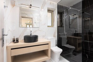 Ein modernes Badezimmer mit Marmorwaschtisch, Waschbecken in Schwarz, Toilette und einer Duschkabine.