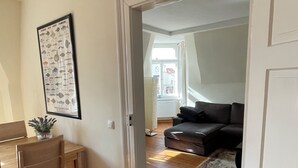 Een kamer met een houten vloer, een eettafel met stoelen, een zwarte bank en een lijst met een afbeelding aan de muur.