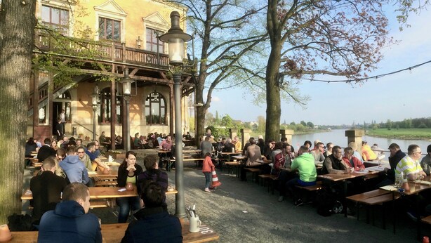 Een buiten eethoek met houten tafels en banken, met uitzicht op een waterpartij.