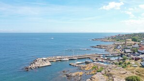 Un pueblo costero con un puerto rocoso, barcos y un muelle que se adentra en el mar.