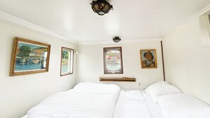 Una habitación con dos camas, una ventana con vista a barcos y tres cuadros en las paredes.