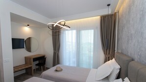 Een hotelkamer met twee bedden, een bureau, een stoel, een televisie en uitzicht op de stad door grote ramen.