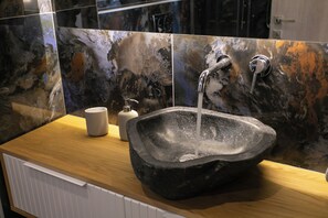 A stone sink with running water, a white soap dispenser, and a beige mug on a wooden countertop. - Elais Luxury Villas (Parga)