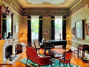 A grand room with a piano, a fireplace, and a large window with curtains.