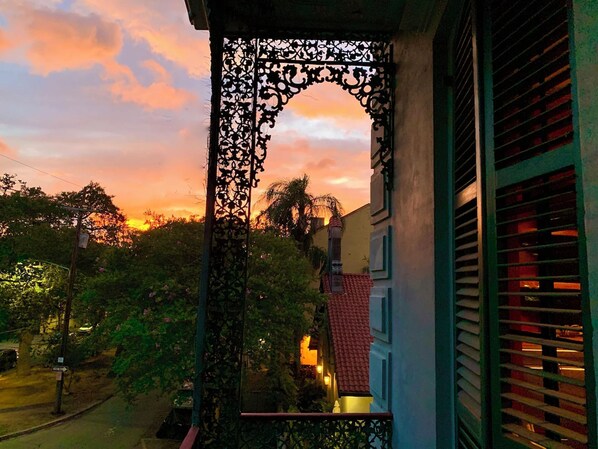 A balcony with a wrought iron gate, a red-tiled roof, and a view of the sunset.