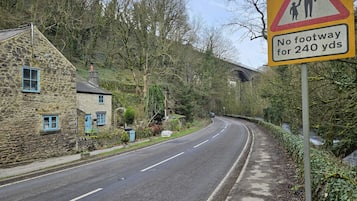 A rural road with a 'No footway for 240 yds' sign, stone houses, and a bridge in the background.