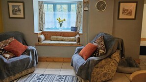 A cozy living room with two armchairs, a wooden bench, and a window with lace curtains. - Rose Cottage - Cosy Cottage in Millers Dale (Buxton)