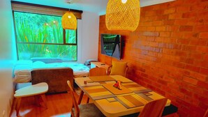 A cozy room with a wooden dining table, chairs, a sofa, and a large window with a view of greenery. - Unbeatable Quality and near to the forest ! (Bogotá)
