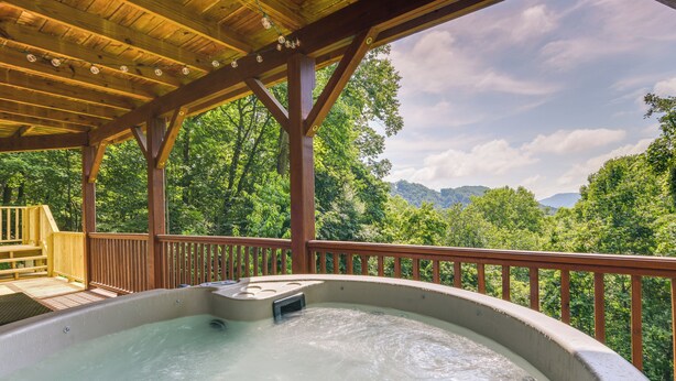 Un jacuzzi bajo una terraza de madera con vistas a un bosque y montañas.