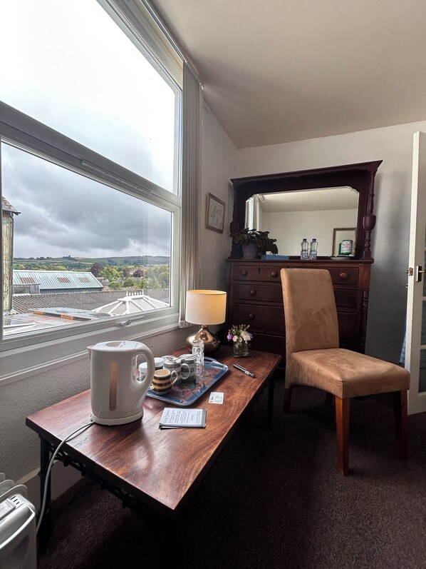 Habitación de hotel con un escritorio de madera, una silla, un ventanal con vistas al campo, un espejo y una lámpara.