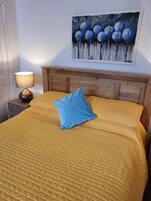 Una cama con un edredón amarillo, una almohada azul y un cabecero de madera.