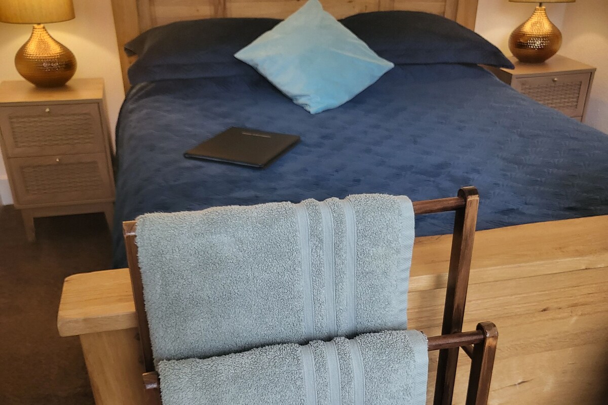 Una cama de madera con una colcha azul y una sola almohada, flanqueada por dos mesitas de noche con lámparas.