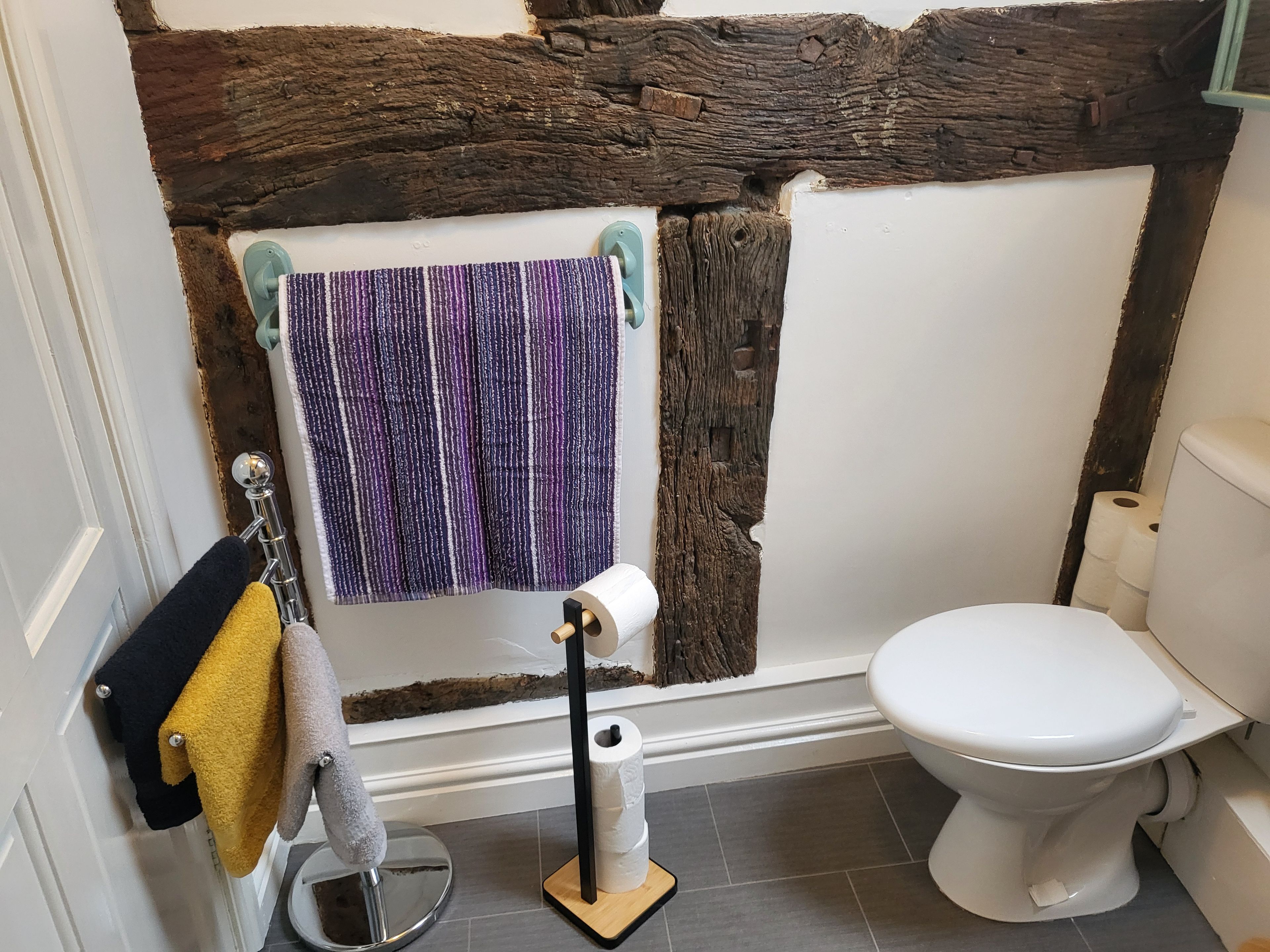 Un baño con inodoro blanco, toallero con toallas y un rollo de papel higiénico.