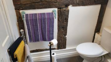 Un baño con inodoro blanco, toallero con toallas y un rollo de papel higiénico.